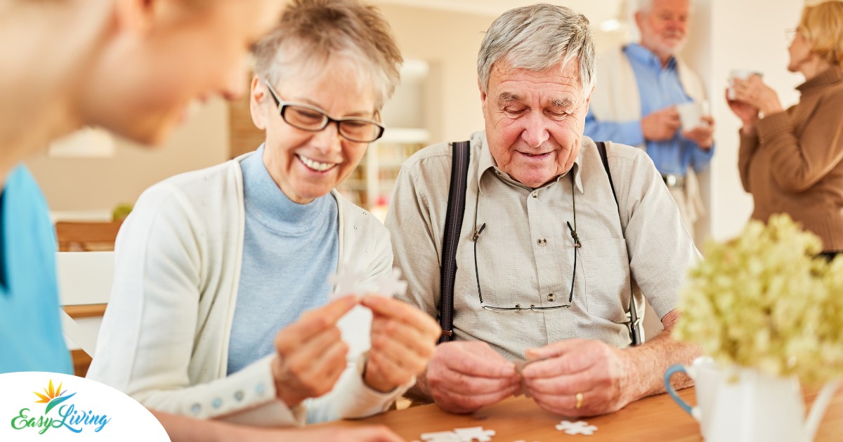 An older couple works on a puzzle with a caregiver, representing the kind of activity that helps those with dementia and also representing Alzheimer’s and Brain Awareness Month.
